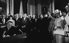 President Lyndon B. Johnson signs the Voting Rights Act of 1965 while Martin Luther King and others look on.