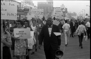 African American and white Mississippi Freedom Democratic Party supporters holding signs reading "Freedom now" and "MFDP supports LBJ" while marching on the boardwalk at the 1964 Democratic National Convention, Atlantic City, New Jersey