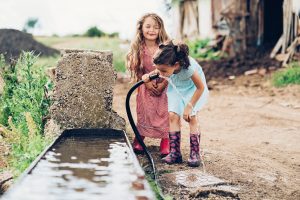 Two children drinking water outdoors. An estimated 110 million Americans are potentially exposed to PFAS through drinking water.