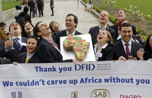 WDM campaigners dressed as business people from Monsanto, Diageo, SABMiller and Unilever deliver a cake to the Department for International Development to thank the UK government for its support to allow them to carve up Africa.