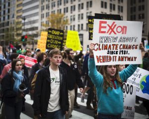 Climate activists demonstrate in Washington, D.C. in 2015. One displays a sign admonishing ExxonMobil for its complicity in furthering the climate apocalypse.