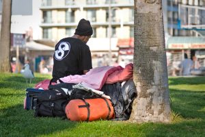 A homeless man sits in the shade with his belongings at Venice Beach. Apple's pledge to stem California's housing crisis is being criticized for not tackling homelessness.